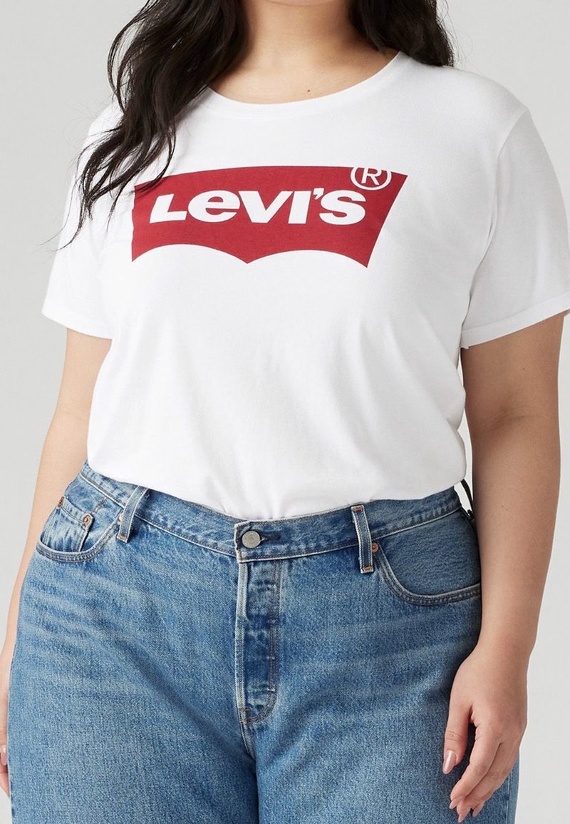 T-shirt en coton blanc avec un logo rouge Levi's imprimé au centre. Associé à un jean en denim bleu taille haute, affichant une coupe classique.