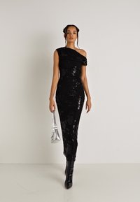 Melna, bez piedurknēm kleita ar asimetrisku dekoltē, ziedu tekstūru, piegulošu siluetu, savienota ar sudraba rokassomu un ceļgala augstuma zābakiem.