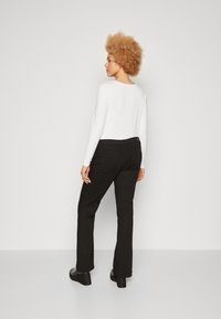 Haut à manches longues blanc et pantalon noir ajusté. Les pantalons ont des poches arrière et un léger évasement en bas. Tissu lisse avec une finition élégante.