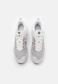 Weiße Sportschuhe mit einem strukturierten grauen Obermaterial, roten Akzenten und einer weißen Sohle. Mit einem Schnürdesign und einem Logo auf der Zunge.
