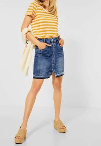 Jeanskjol med framknappar, med en lätt opiffning vid fållen. Kombinerad med en randig T-shirt i orange och vitt samt kilklack-sandaler.