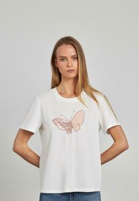 Camiseta de algodón blanca con mangas cortas que presenta un bordado de mariposa rosa en el frente. Corte sencillo y relajado con escote redondo.