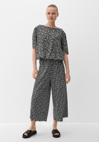 Schwarzes Oberteil mit Blumenmuster in lockerer Passform, weit geschnittene passende Hose und schwarze Rutschsandalen. Leichtes Material, entspannte Silhouette.