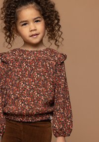 Bloes met bloemmotief en gerimpelde mouwen, voornamelijk in tinten oranje en bruin, gemaakt van een gestructureerde stof met een gather hem.