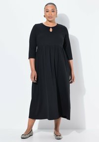 Mustat polvipituiset mekko, jossa on pyöreä pääntie ja avainreiän yksityiskohta, 3/4 hihalla ja kerätty vyötärö. Yhdistetty kuvioituihin ballerinoihin.