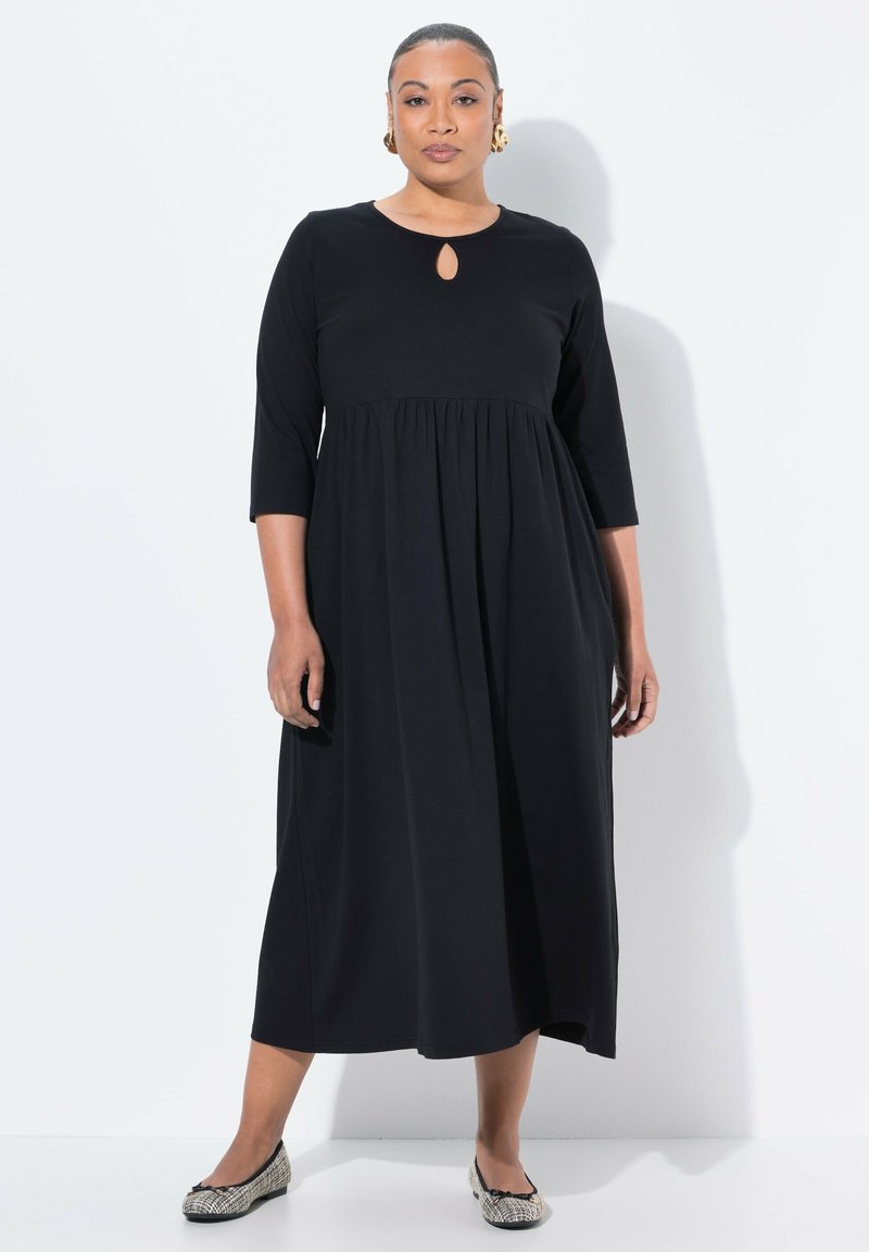 Mustat polvipituiset mekko, jossa on pyöreä pääntie ja avainreiän yksityiskohta, 3/4 hihalla ja kerätty vyötärö. Yhdistetty kuvioituihin ballerinoihin.