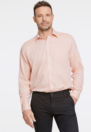 Helles rosa Hemd mit Knopfleiste, Brusttasche und gemustertem Innensaum, kombiniert mit schwarzen, lässig geschnittenen Hosen aus glattem Stoff.