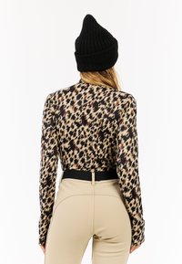 Langärmliges Oberteil mit Leopardenmuster in Braun- und Schwarztönen, kombiniert mit beigefarbenen High-Waist-Hosen und einer schwarzen gerippten Strickmütze.