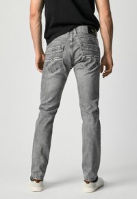 Vaqueros de mezclilla gris con un corte slim, que cuentan con bolsillos traseros con costuras distintivas y un parche de cuero. Combinados con zapatillas blancas y marrones.