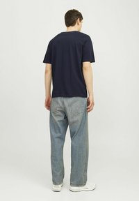 Tricou din bumbac de culoare bleumarin, cu mâneci scurte, guler rotund și croială lejeră, asociat cu blugi din denim deschis, cu o croială liberă.