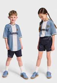 Lichtblauw en wit sportshirt met zwarte accenten, gecombineerd met donkere korte broek. Beiden dragen blauwe sneakers en witte sokken. Voorzien van logo en tekst.