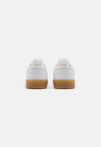 White leather sneakers with a gum rubber sole. Includes "BOSS" branding on the heel in orange. Features a smooth, minimalist design.