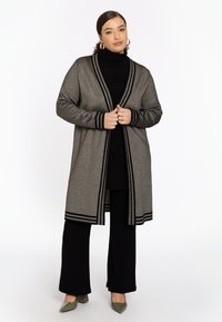 Grau Cardigan mit schwarzen Streifenakzenten, langen Ärmeln, offenem Vorderteil und knielanger Schnitt, getragen über einem schwarzen Rollkragenpullover und Hose.