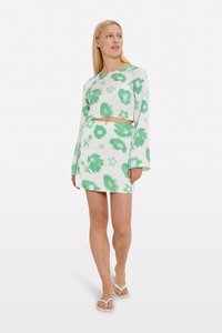 Haut court à motifs floraux verts et jupe assortie en tissu texturé. Le haut arbore des manches longues et un col rond.
