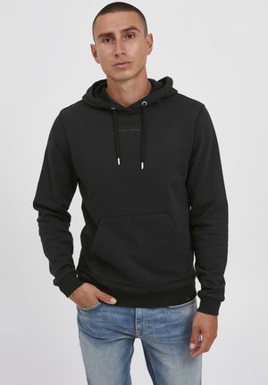 Svart hooded sweatshirt med framficka, ribbade ärmslut och en subtil logotyp tryckt på bröstet. Bärs med ljusblå jeans.