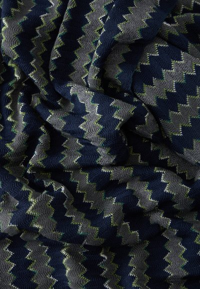 Tissu tricoté à motif zigzag bleu foncé et gris avec des accents subtils verts et blancs, présenté avec de doux plis et une texture.