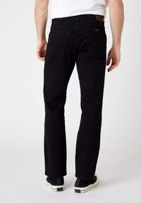 Jeans in denim nero con design a gamba dritta, cinque tasche e dettagli di cucitura sottili. Indossati con calzature scure e una camicia bianca.