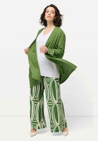 Zelený lehký kimono top přes bílý tričko, spárovaný s širokými kalhotami s vzorem v zelené a smetanové barvě se geometrickým designem.
