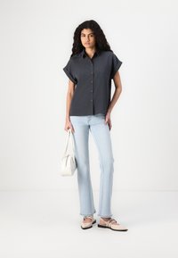 Tumši pelēks īsām piedurknēm pogājams krekls ar divām krūšu kabatām, apvienots ar gaiši ziliem platām biksēm un rozā slip-on apaviem. Balta rokassoma rokā.