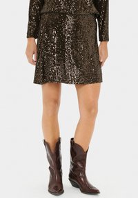 Falda mini de lentejuelas marrón con una cinturilla ajustada, combinada con botas de vaquero marrones hasta la rodilla con punta afilada y diseño angular.