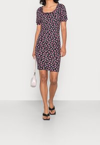 Czarna sukienka w kwiaty z krótkimi bufkami, kwadratowym dekoltem i dopasowanym krojem. W połączeniu z małą różową torebką i czarnymi sandałami.
