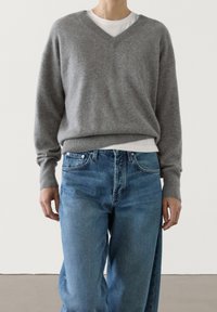 Gray wool v-neck sweater with long sleeves, worn over a white t-shirt; paired with light blue denim jeans featuring a classic cut.