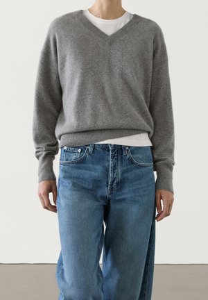 Gray wool v-neck sweater with long sleeves, worn over a white t-shirt; paired with light blue denim jeans featuring a classic cut.