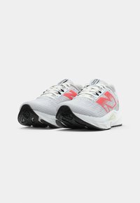 Des chaussures de course grises et blanches avec un dessus texturé, ornées d'accents roses et d'une semelle en caoutchouc noire, conçues pour la stabilité et le confort.
