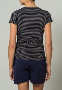 Pasiasta czarno-szara koszulka z krótkim rękawem i marszczeniami po bokach, w połączeniu z granatowymi szortami. Gładka faktura i dopasowany krój.