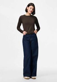 Top marrón de manga larga combinado con pantalones de mezclilla de pierna ancha en azul oscuro. La mezclilla presenta una textura sutil e incluye bolsillos frontales.