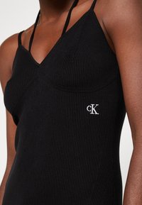 Svart ribbad linne med smala axelband och v-ringning. Har en vit "ck" logo på vänster sida. Mjuk textur och figurnära design.