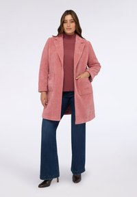 Rosa strukturierten Mantel mit einem Reverskragen, Vordertaschen und langen Ärmeln, kombiniert mit einem bordeauxfarbenen Oberteil und dunkelblauen Schlagjeans.