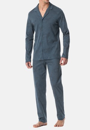 Mann in blauem, gemustertem Langarm-Pyjama-Oberteil und passenden Hosen, barfuß vor einem weißen Hintergrund stehend.