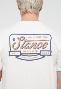 White t-shirt featuring a large graphic on the back in blue and tan, with the text "The Original Stance MFG Co." and "2009."