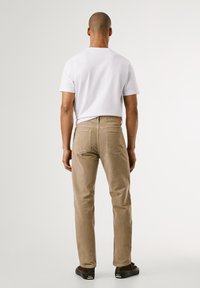 Pantaloni in corduroy per uomo di colore marrone chiaro, con un design a gamba dritta e due tasche posteriori. Abbinati a una t-shirt bianca semplice a maniche corte.
