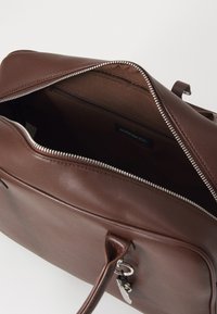 Brown leather bag with a smooth texture, silver zipper, and an inner pocket. The interior is a darker shade, featuring brand labeling inside.