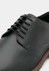Pantofii de dress din piele gri, cu un finisaj neted, prezentând un design clasic cu șireturi, detalii de cusătură subtile și o talpă de culoare maro deschis.