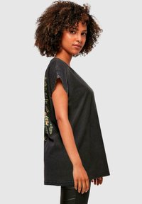 Schwarzes, oversized T-Shirt mit kurzen Ärmeln, das einen bunten Grafikdruck zur Seite zeigt. Weiches, leicht strukturiertes Baumwollmaterial.