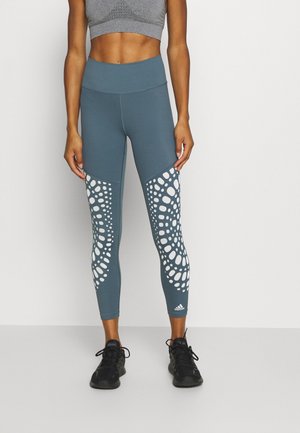 Leggings teal avec une taille haute et un motif perforé blanc sur le bas des jambes. Fabriqués dans un matériau extensible, conçus pour le confort lors des activités.