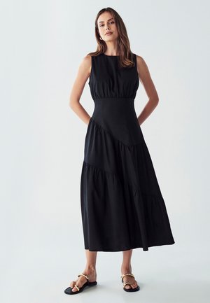 Schwarzes Baumwoll-Maxikleid mit tailliertem Oberteil, gestuften Rock und ärmellosem Design. Akzentuiert mit einem Taillenbund und fließender Textur.