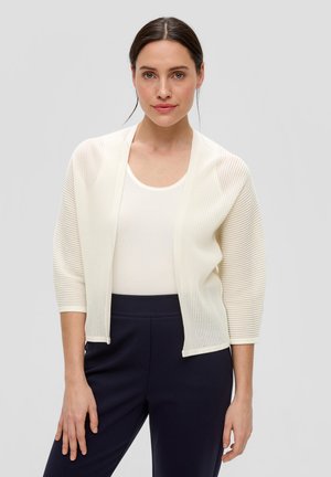 Lichte, geribde cardigan in off-white, open voorkant met driekwartmouwen, gecombineerd met een aansluitend wit topje en donkerblauwe broeken.