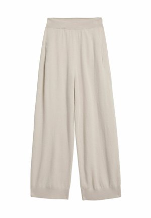 Kvinde står barfodet iført beige ærmeløs crop top og matchende vidbenede strikkede bukser mod en ensfarvet baggrund.