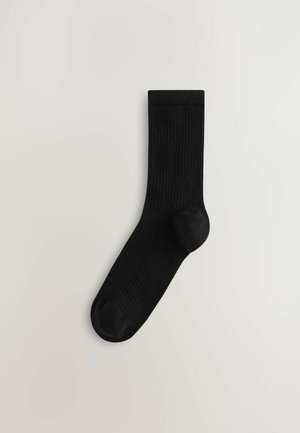 Chaussette noire côtelée avec un orteil arrondi et une bande supérieure sans couture, fabriquée à partir d'un matériau doux et extensible pour le confort.