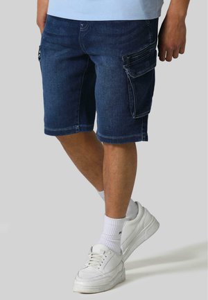 Denim cargo shorts in donkerblauw met meerdere zakken, gestikte randen en een gewone pasvorm. Gecombineerd met witte sneakers en ribbelige sokken.