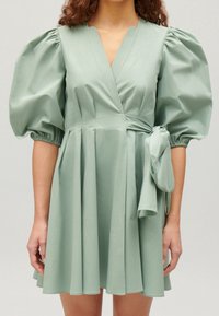 Zelené šaty s krátkým rukávem vyrobené z hladké tkaniny, s nabíranými rukávy, zavinovacím designem a uvázaným akcentem v pase.