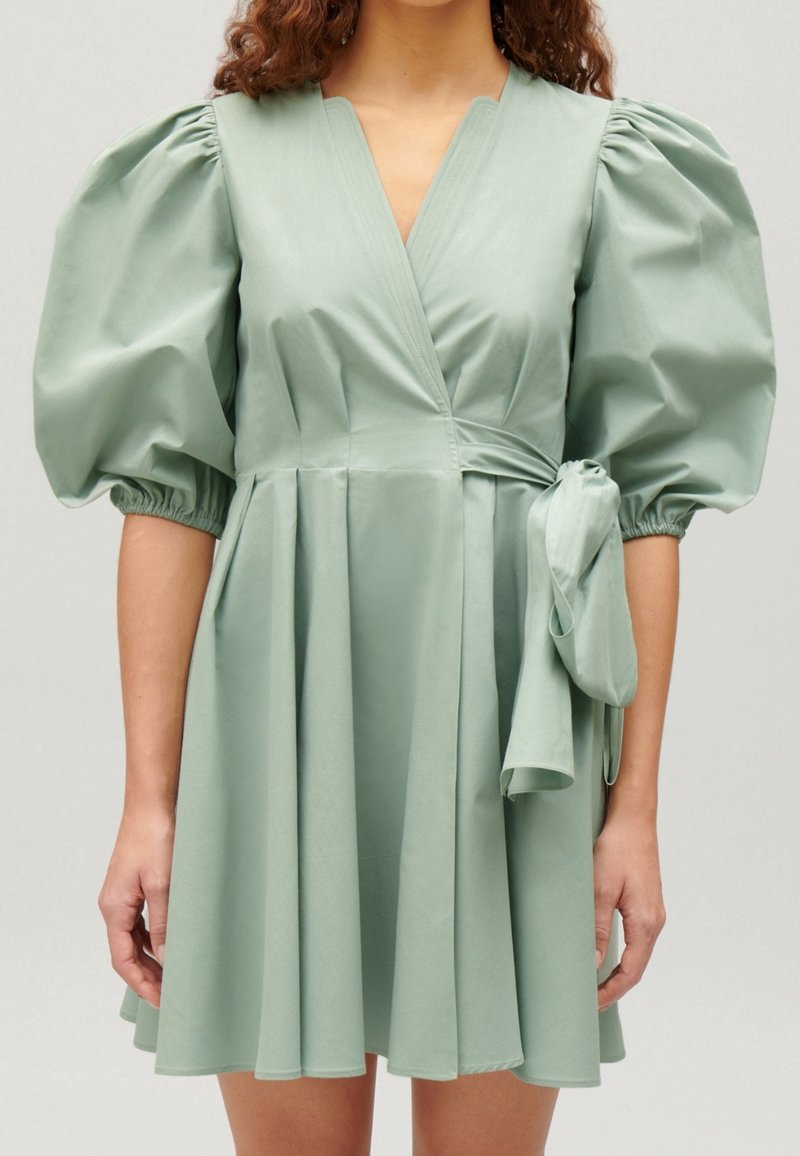 Zelené šaty s krátkým rukávem vyrobené z hladké tkaniny, s nabíranými rukávy, zavinovacím designem a uvázaným akcentem v pase.