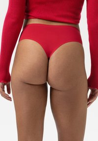 Rote nahtlose Bikiniunterwäsche mit glatter Textur, hochgeschnittenem und tief sitzendem Design, von hinten vor einem weißen Hintergrund betrachtet.