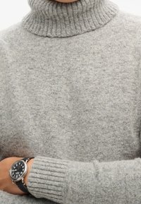 Grijze gebreide coltrui met een geribbelde kraag en manchetten, met een zachte textuur; gedragen met een zwart horloge met witte cijfers.