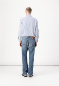 Light blue, striped long-sleeve shirt paired with light blue jeans. Jeans feature a red brand label and two back pockets. Sneakers visible.