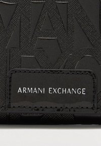 Črn denarnica z embosiranim logotipom, teksturirano površino in pravokotno oznako, na kateri v belih črkah piše "ARMANI EXCHANGE".